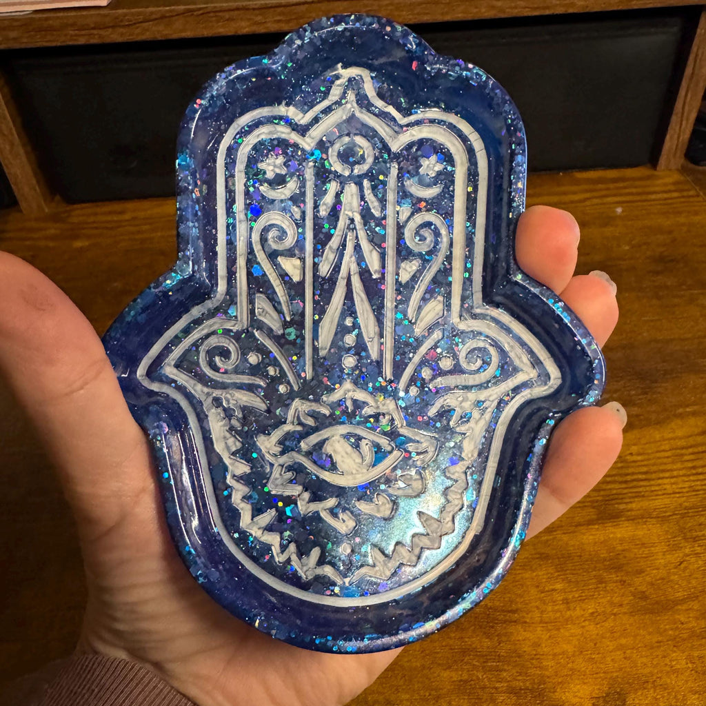 Hand holding a blue and white Hamsa hand patch on a wooden surface