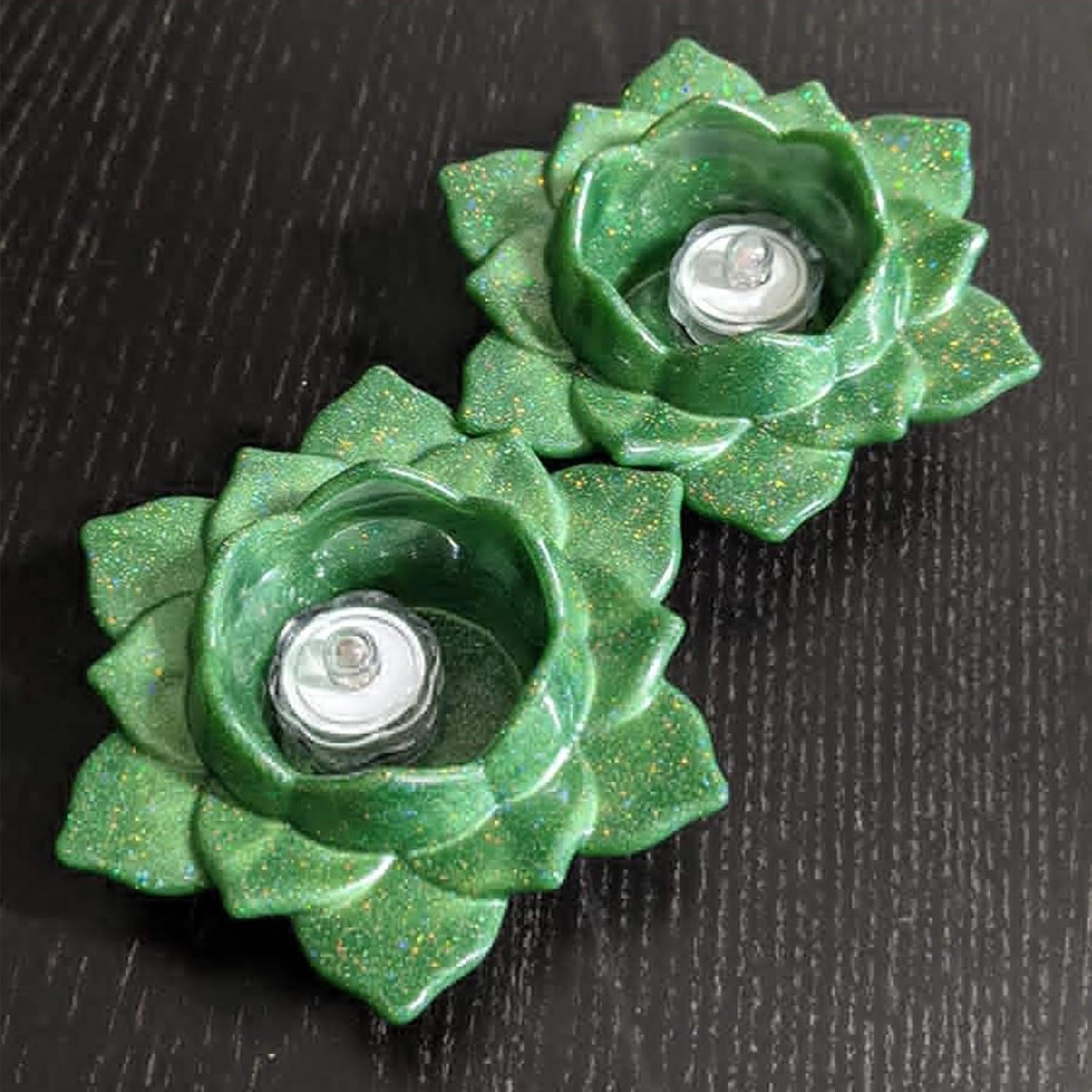 Two green flower-shaped candle holders on a dark surface