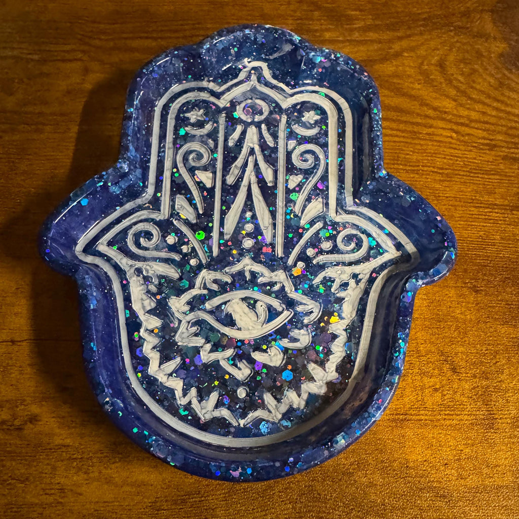 Decorative Hamsa hand with blue glittery border on a wooden surface